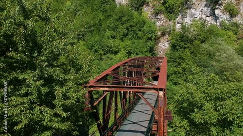 Old railway bridge leading to the mountain cliffs surrounded by trees and other vegetation. Aerial drone descending shot photo