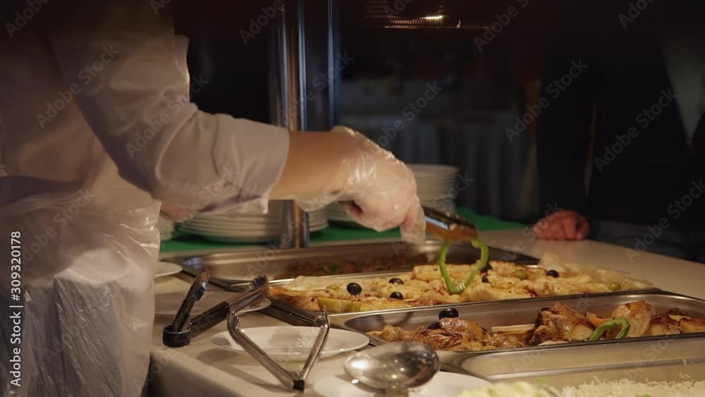 cafeteria worker puts meat on plate and gives it to customer. servicing food that buyer chooses. in modern canteen, cafe, public catering, mess hall. close-up of cafeteria assortment.