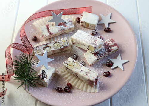 Primo piano dei torroncini molli con frutti di bosco su un piatto con decorazioni natalizie. Sfondo bianco photo