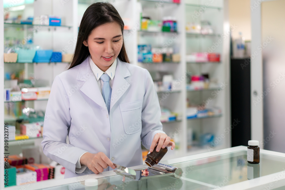 Asian young woman pharmacist pour and count drug capsules on stainless tray, she prepare drug pack to patient in the pharmacy drugstore. Medicine, pharmaceutics, health care and people concept. Asian young woman pharmacist pour and count drug capsules on stainless tray, she prepare drug pack to patient in the pharmacy drugstore. Medicine, pharmaceutics, health care and people concept.