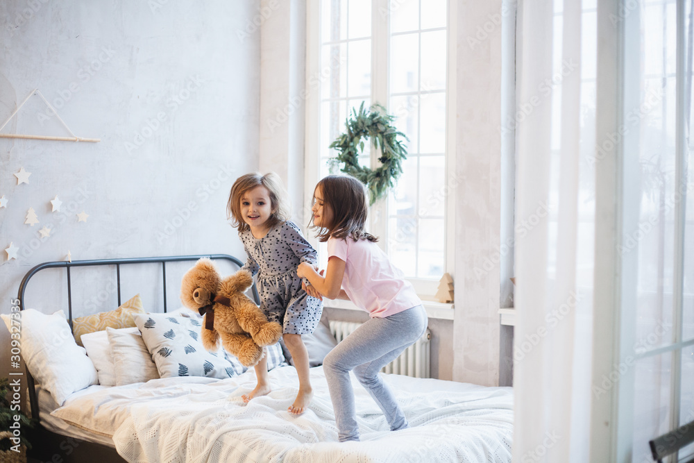 Two girls, sisters fighting pillows on the bed, the window decorated with a Christmas wreath, life, childhood Two girls, sisters fighting pillows on the bed, the window decorated with a Christmas wreath, life, childhood