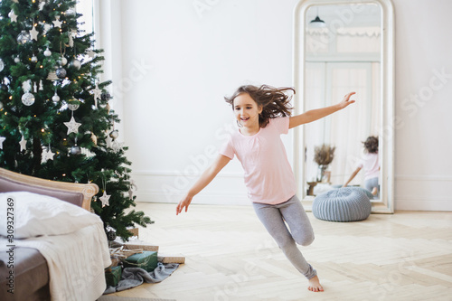 Girl runs around the room decorated for the new year, Christmas tree