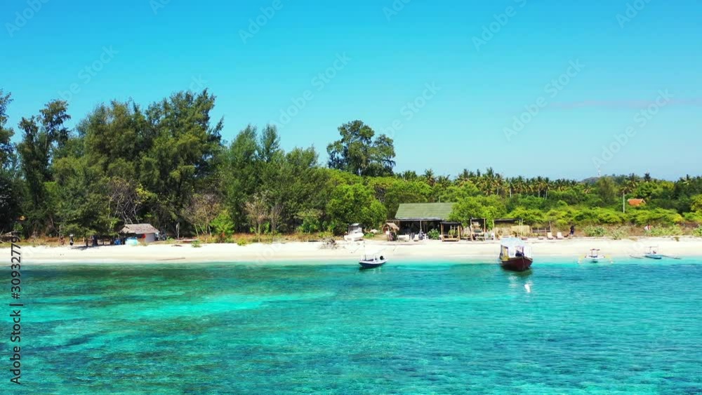Quiet exotic beach with white sand bordered by green tropical trees and turquoise lagoon with clear calm water where fishing boats floating in Jamaica Quiet exotic beach with white sand bordered by green tropical trees and turquoise lagoon with clear calm water where fishing boats floating in Jamaica
