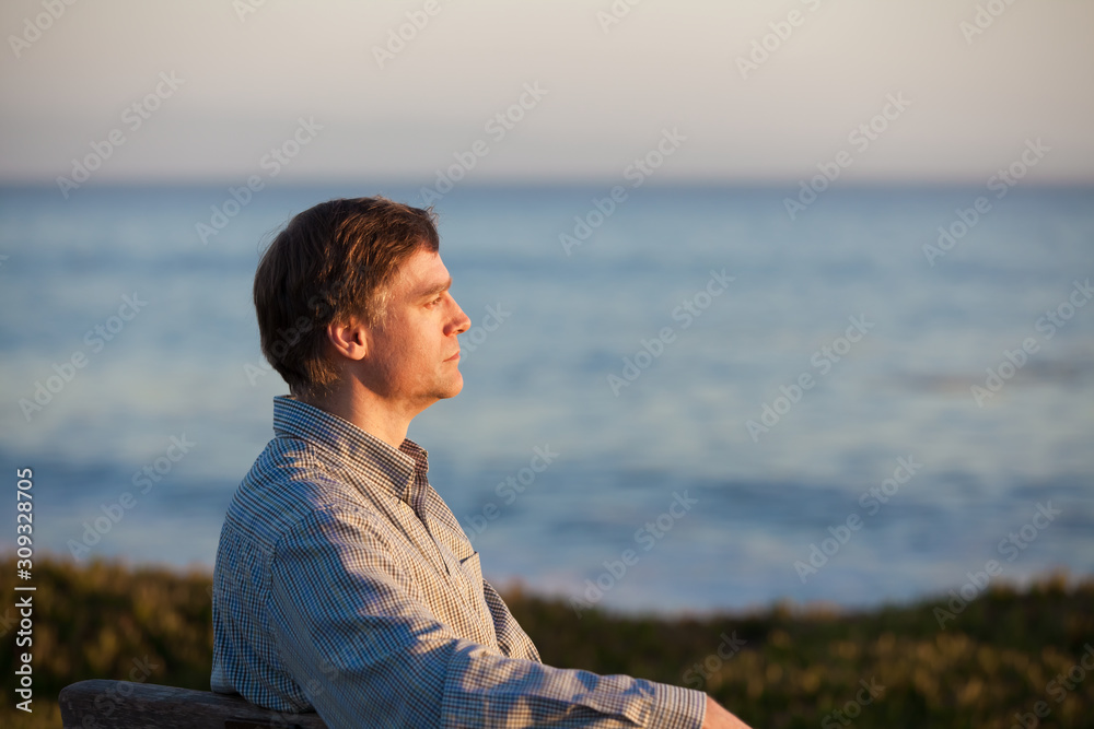 Profile of Caucasian man in 50s by ocean at sunset
