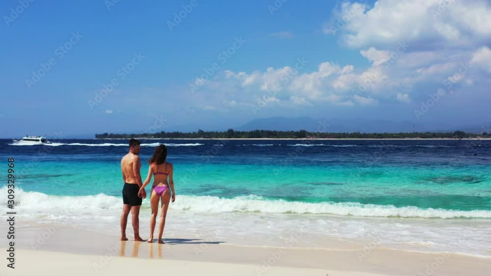 A young romantic couple enjoying tropical honeymoon, Sandy beach, foamy waves and yacht sailing on the sea A young romantic couple enjoying tropical honeymoon, Sandy beach, foamy waves and yacht sailing on the sea