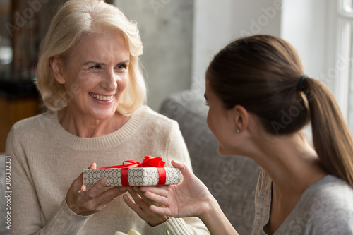 Adult daughter present gift box to smiling senior mom