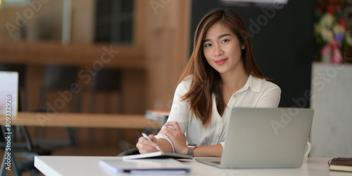 Young beautiful asian businesswoman working on her project with laptop computer and smiling to the camera