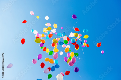 Colorful multicolored inflatable balls fly in air against background blue sky during festive festival. Salute in sky from colorful balloons. Happy holiday background
