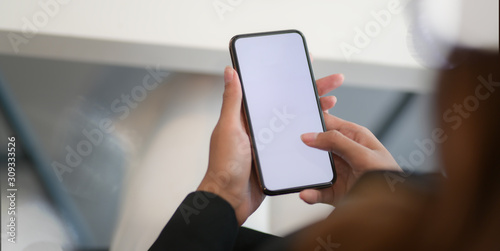 Close-up view of young businesswoman using blank screen smartphone while working on the project