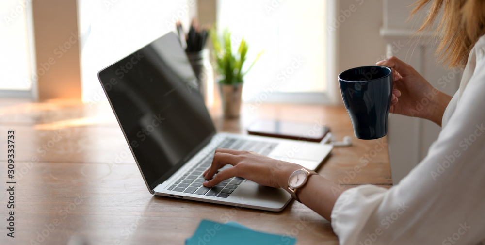 Close-up view of young beautiful businesswoman working on her project while drinking a coffee cup in comfortable office Close-up view of young beautiful businesswoman working on her project while drinking a coffee cup in comfortable office