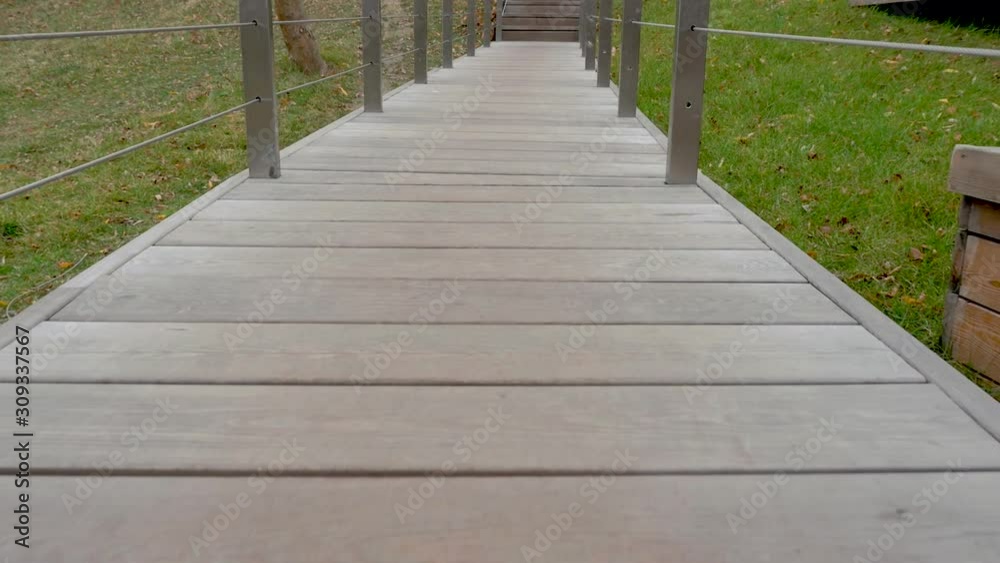 the camera moves slowly along the narrow wooden deck. The sides of the railing. ahead of the stairs. On the sides of the green grass and yellow leaves. Autumn. Dull. Day. the camera moves slowly along the narrow wooden deck. The sides of the railing. ahead of the stairs. On the sides of the green grass and yellow leaves. Autumn. Dull. Day.