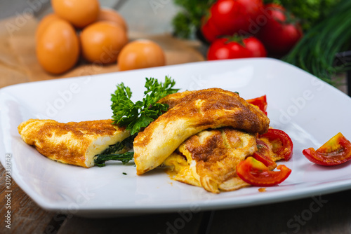 Traditional omelet with vegetables, spinach, tomatoes and herbs on a wooden table in a restaurant.