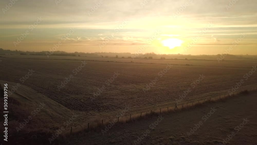 Drone flies up and backwards, away from warm sunrise, across frosty fields. Reveals beautiful landscape and cloud formation as drone flies up. Drone flies up and backwards, away from warm sunrise, across frosty fields. Reveals beautiful landscape and cloud formation as drone flies up.