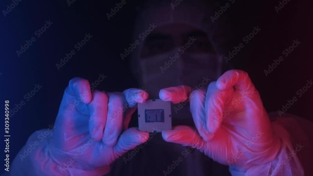 technician engineer in a lab wearing sterile gloves holds a computer processor in neon light with his fingers. Scientific and industrial developments in biometrics. Production of computer chips. technician engineer in a lab wearing sterile gloves holds a computer processor in neon light with his fingers. Scientific and industrial developments in biometrics. Production of computer chips.