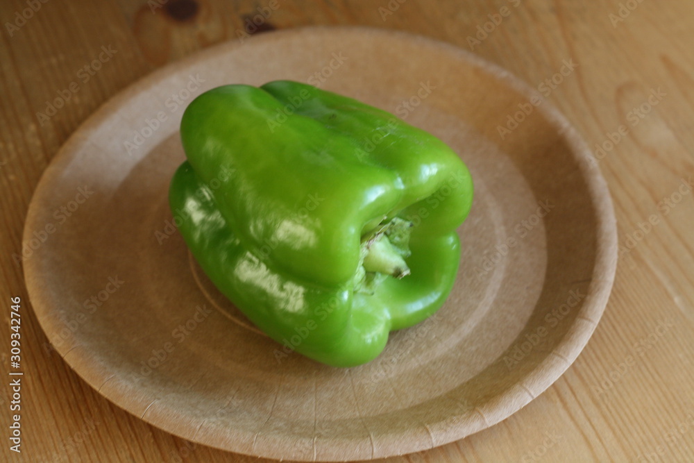 Green sweet pepper in a paper plate on a wooden table Green sweet pepper in a paper plate on a wooden table
