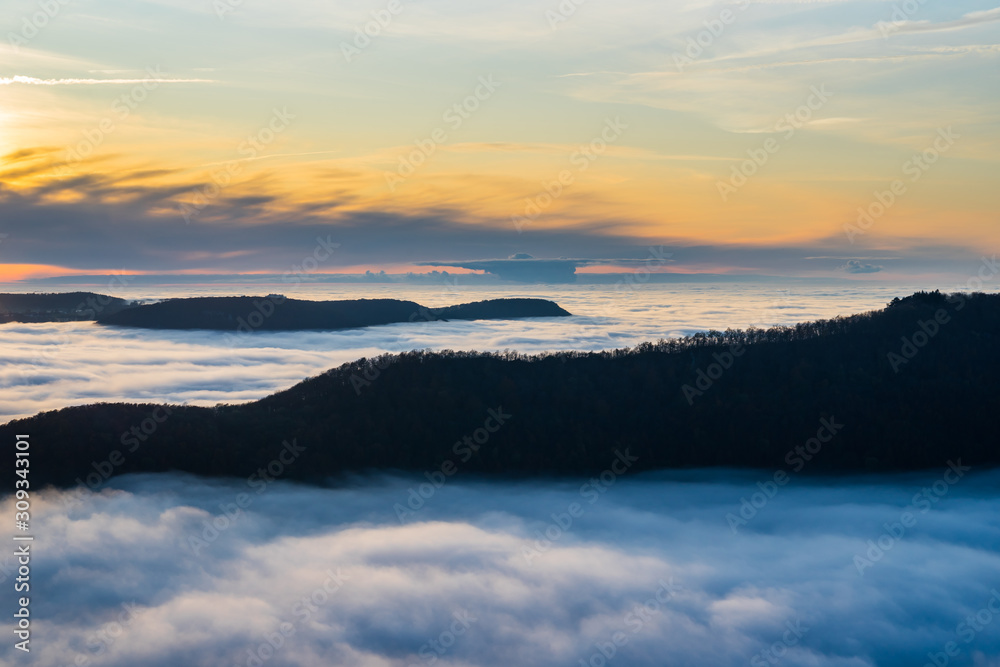 Germany, Majestic aerial view above endless fog clouds in valley of swabian jura nature landscape at sunset with orange sky near stuttgart on mountain breitenstein