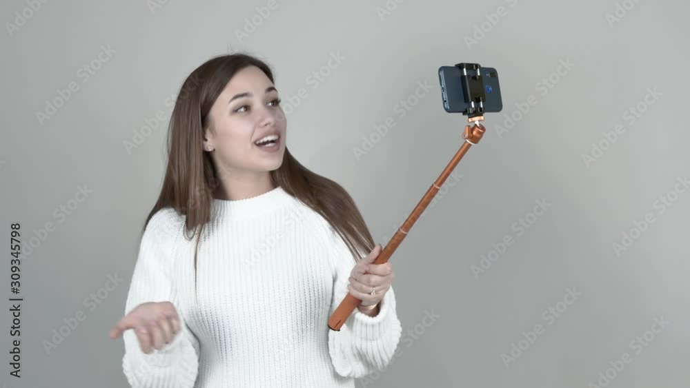 Grey background Caucasian girl blogger white cardigan long straight hair brown haired holding cellphone talking, smiling, holding hand to chest, communicating with followers