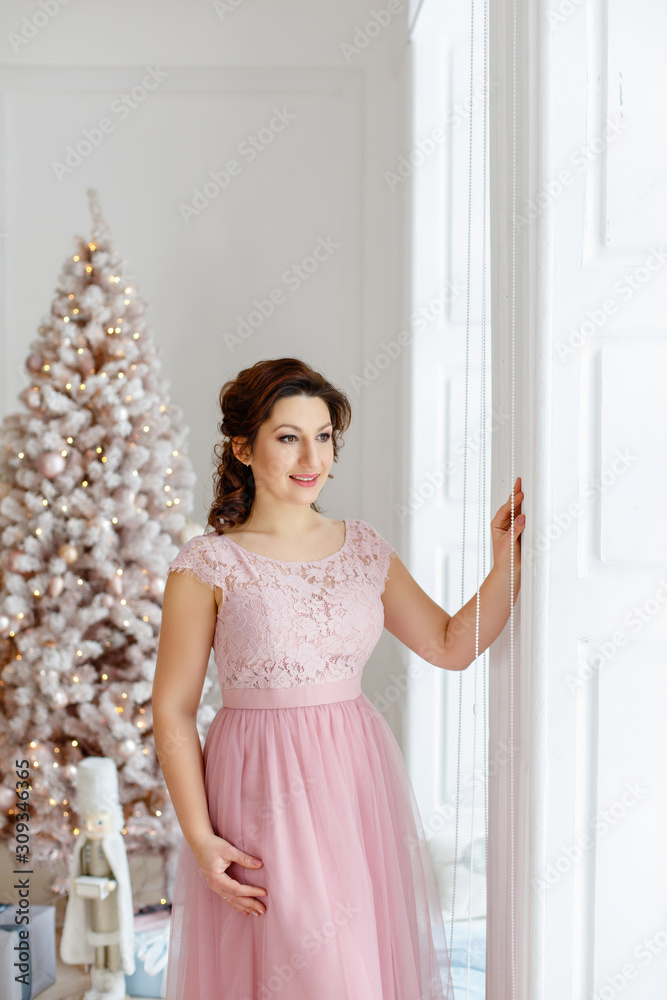 Young woman in romantic pink room decorated for christmas and new year. Pink dress for celebrting christmas. smile and happy