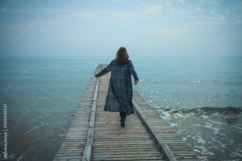 Young Girl Walking on the Pier to the Sea Young Girl Walking on the Pier to the Sea