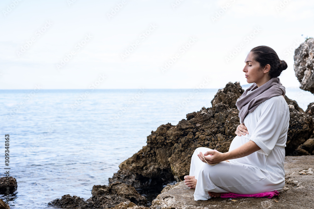 Beautiful pregnant woman is meditating on the beach