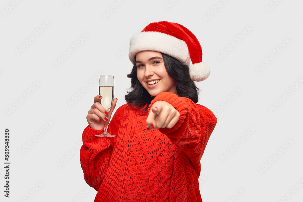 Beautiful brunette girl in a red sweater and Santa hat holding glass of champagne. Beautiful brunette girl in a red sweater and Santa hat holding glass of champagne.