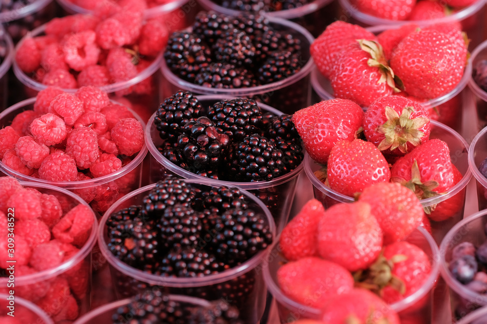 A counter with plastic containers and glasses filled with fresh berries. Blackberry, Strawberry, Blueberry, Raspberry. Food market. A counter with plastic containers and glasses filled with fresh berries. Blackberry, Strawberry, Blueberry, Raspberry. Food market.