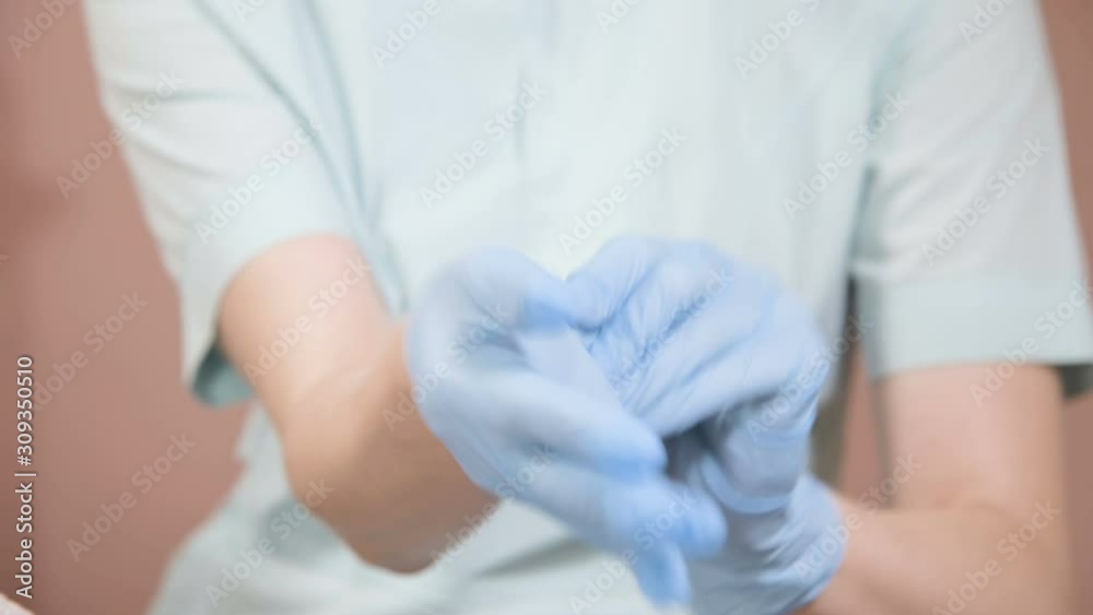 Close-up Professional woman beautician puts on her hands blue rubber clean sterile gloves before doing the procedure for cosmetic skin care of the client's face. Close-up Professional woman beautician puts on her hands blue rubber clean sterile gloves before doing the procedure for cosmetic skin care of the client's face.