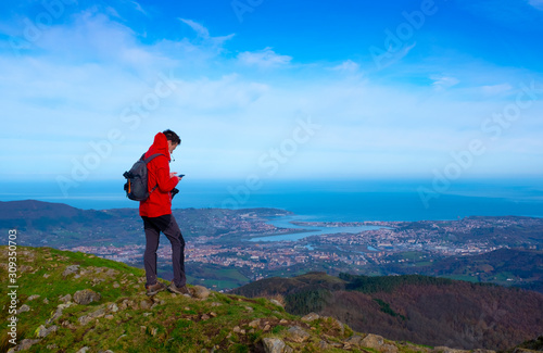Man with cellphone in his hand on the mountain and the city in the background, Aiako Harriak Natural Park, Euskadi