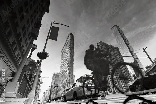 Manhattan in puddle reflection with pedestrians, bicycle, taxi, Flatiron building.