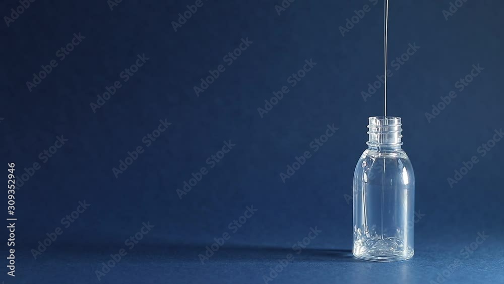 Thick transparent liquid pours into empty plastic container on dark blue background. Cosmetic product (gel or shampoo) fills travel bottle Thick transparent liquid pours into empty plastic container on dark blue background. Cosmetic product (gel or shampoo) fills travel bottle