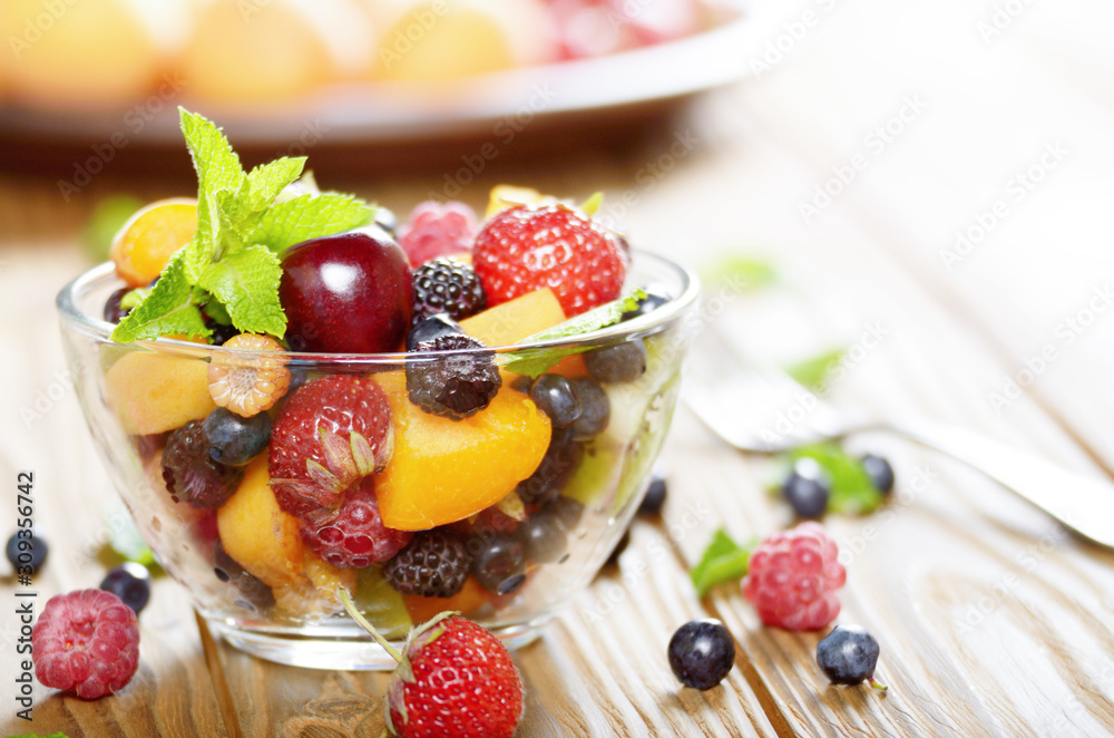 Assorted fruits in glass bowl on kitchen wooden table with fork aside Assorted fruits in glass bowl on kitchen wooden table with fork aside