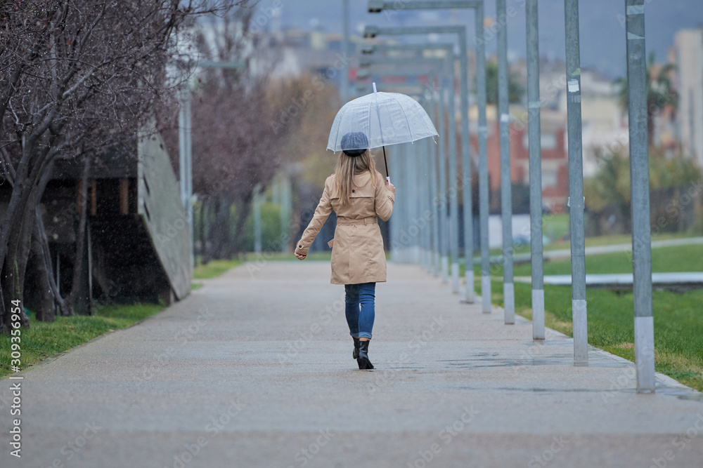 A girl walking through a park, with a transparent umbrella because it rains, is on her back