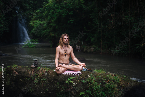 Yoga practice and meditation in nature. Man practicing near river © grthirteen