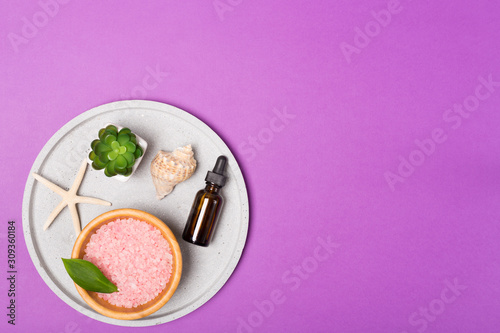 Beauty and spa concept. Sea salt, oil, green leaves and shells on grey tray on purple background. Flat lay. Copy space. 