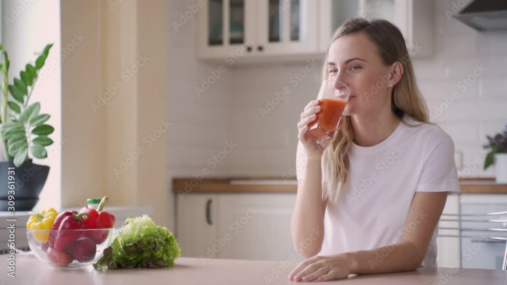 Woman drinking carrot juice in the kitchen Woman drinking carrot juice in the kitchen