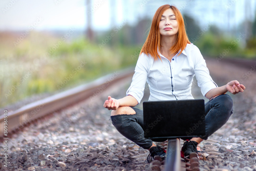 Young and beautiful asian woman working and meditation with laptop while sitting outdoor on the rails Young and beautiful asian woman working and meditation with laptop while sitting outdoor on the rails