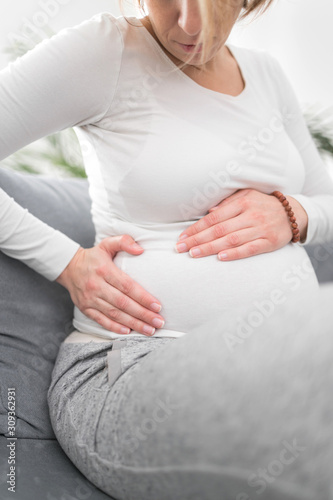 Pregnant tired exhausted woman with stomach issues at home on a couch, being sick.