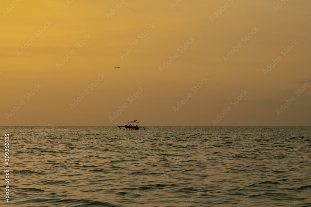 Small fishing boat above which airliner flies at sunset.