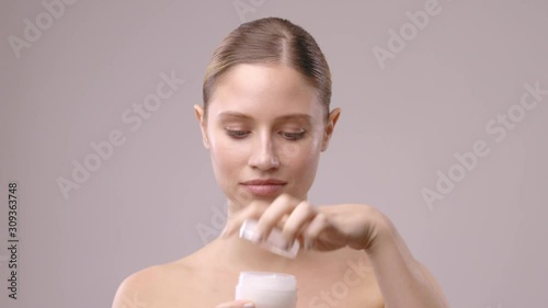 Beautiful blond young woman opening cream and putting it on her pure skin.