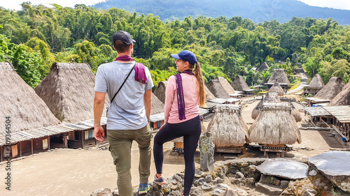 A couple with a purple scarfs admiring the Beno village in Flores, Indonesia. There are many small houses behind him. Each house is made of natural parts like wood and straw. History and tradition photo