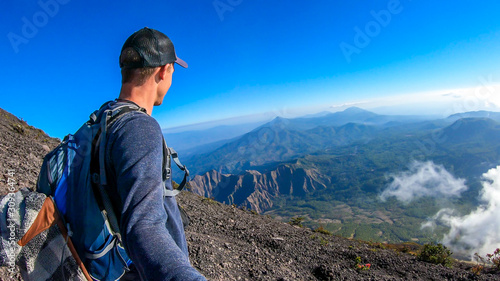 A young man walking down the volcano Inierie in Bajawa, Flores, Indonesia. He takes a selfie while enjoying the beautiful view on volcanic island. Serenity and calmness. Discovering new places photo
