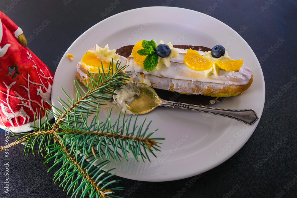Custard with cream on a white plate. The cake is decorated with blueberry, tangerine slices and mint leaves. On a plate a spoon with cream. Festive mood is created by Christmas deer and spruce branch. Custard with cream on a white plate. The cake is decorated with blueberry, tangerine slices and mint leaves. On a plate a spoon with cream. Festive mood is created by Christmas deer and spruce branch.
