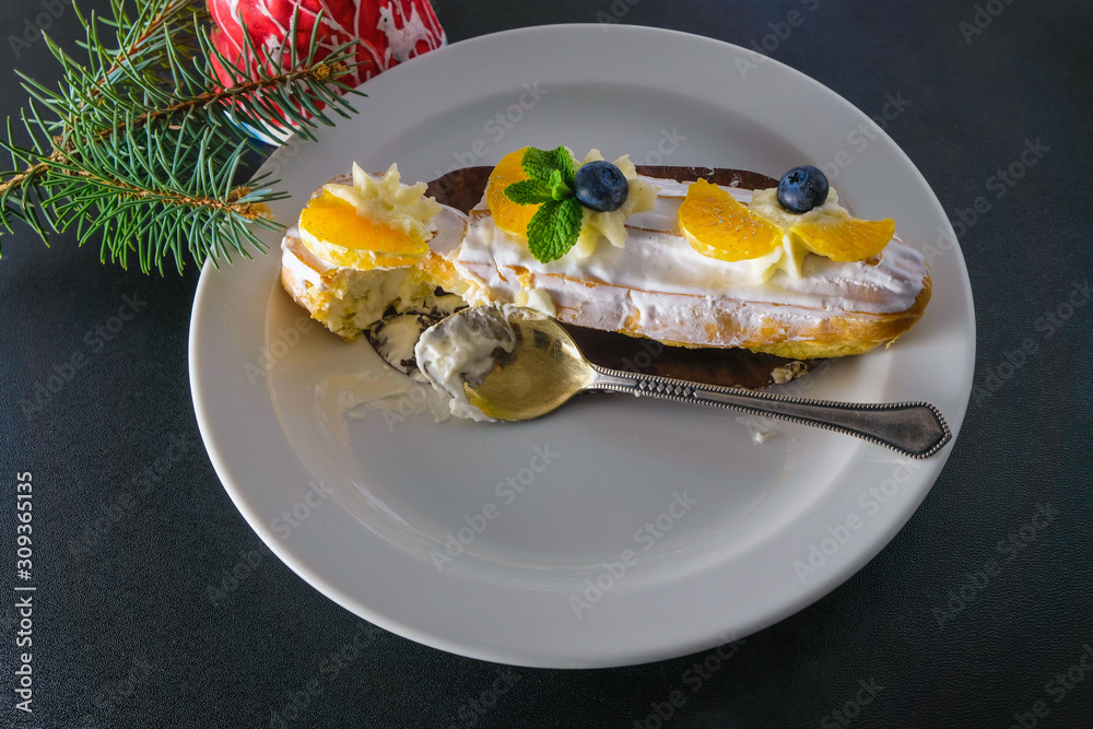 Custard with cream on a white plate. The cake is decorated with blueberry, tangerine slices and mint leaves. On a plate a spoon with cream. Festive mood is created by Christmas deer and spruce branch. Custard with cream on a white plate. The cake is decorated with blueberry, tangerine slices and mint leaves. On a plate a spoon with cream. Festive mood is created by Christmas deer and spruce branch.