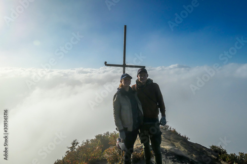 A couple standing on the top of volcano Inierie in Bajawa, Flores, Indonesia, next to a cross. They are surrounded by thick clouds. Sun tries to get through the thick layer of overcast. Freedom. photo