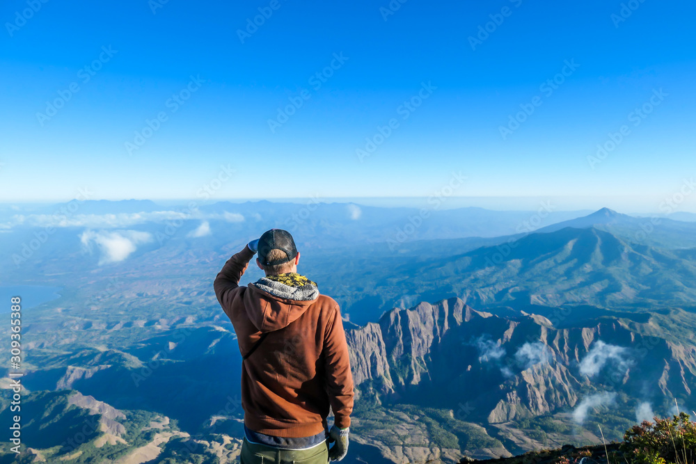 A man standing of the top of volcano Inerie in Bajawa, Flores, Indonesia. He is enjoying the beautiful view on volcanic island. He spreads her hands wide in a gesture of freedom. Clouds around him