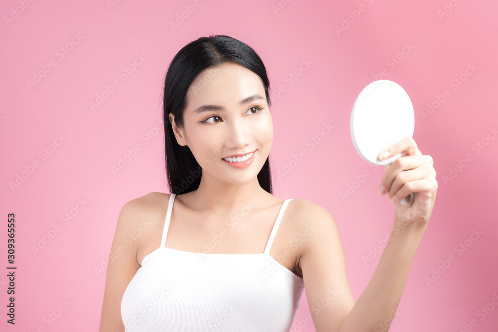 Attractive young Asian woman holding mirror and feeling happy about her skin. Isolated on pink background Attractive young Asian woman holding mirror and feeling happy about her skin. Isolated on pink background