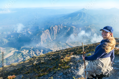 Young woman walking down the steep road on a gravelled volcano Inierie's side in Bajawa, Flores, Indonesia. She supports herself on a wooden stick while enjoying the beautiful view on volcanic island photo