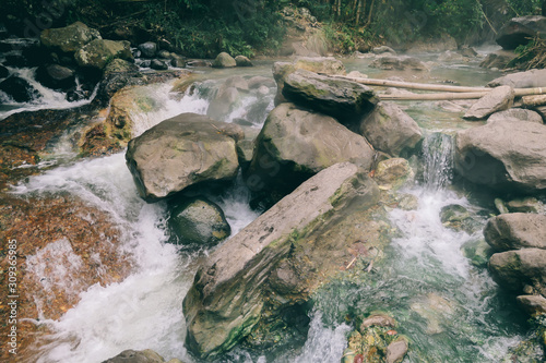 A close up on the hot spring merging with cold river creating a perfect temperature of water in Bajawa, Flores, Indonesia. Banks of the river are overgrown with trees. A lot of moss on the stones photo