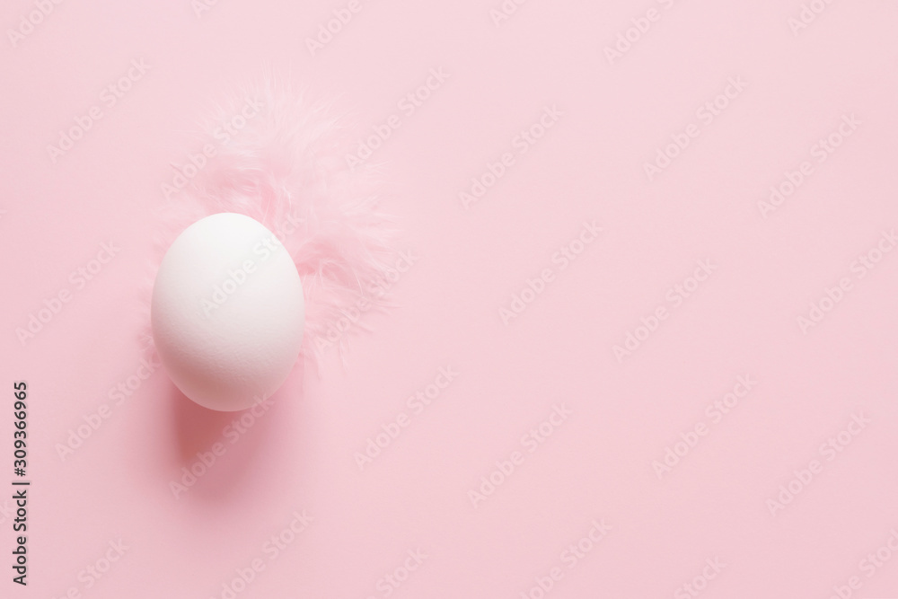 An Easter white egg on a pink feather on pastel pink background with copy space An Easter white egg on a pink feather on pastel pink background with copy space