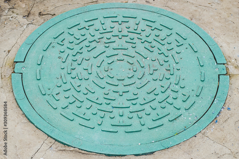 Closed green hatch of sewage at outdoors. Round cover of manhole in concrete, sewer.